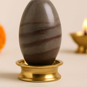 Narmada Shivling on brass stand with diya and marigold – Divine Samagri